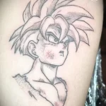 Фото татуировки персонажа Гоку из аниме Dragon Ball на руке. Черно-белый рисунок в стиле аниме. Детализированное изображение лица и волос.