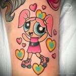 Цветное фото тату с изображением Пузырь из Powerpuff Girls на руке. Яркий и детализированный рисунок в стиле мультфильмов с окружением из сердец.