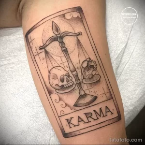 Фото тату: весы правосудия с черепом и сердцем, надпись "KARMA". Рисунок татуировки выполнен в стиле олдскул с использованием четких линий и ярких цветов.