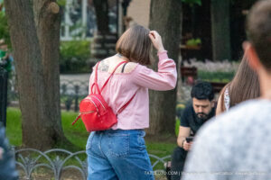 Фото тату: девушка идет по улице с рюкзаком, на спине видна татуировка с изображением птицы. Стильная и современная татуировка.