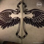 Эскиз татуировки креста с расправленными крыльями, выполненный в стиле олд скул с использованием черных контуров и ярких цветов. Традиционный и выразительный рисунок.