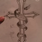 Фото эскиза татуировки креста, обвитого лентой с надписью "Philippians 4:13". Рисунок выполнен в черно-белой гамме с детальной проработкой.