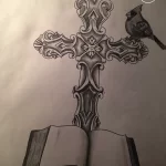 Черно-белый эскиз татуировки креста, стоящего на открытой книге, с сидящей на нем птицей. Символический рисунок веры и знаний.