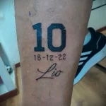 Фото минималистичной татуировки с номером "10" и именем "Leo", выполненной черными чернилами на коже.