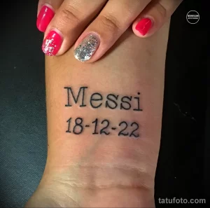 Фото минималистичной татуировки с именем "Messi" и датой "18-12-22", выполненной черными чернилами на коже.