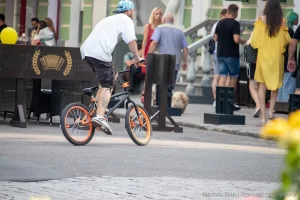 Фотография BMX-райдера на фоне городской архитектуры с видимой татуировкой на руке, демонстрирующей стиль и индивидуальность.