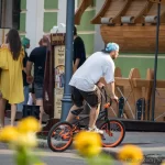Фотография BMX-райдера на фоне городской архитектуры с видимой татуировкой на руке, демонстрирующей стиль и индивидуальность.