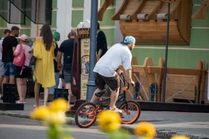 Фотография BMX-райдера на фоне городской архитектуры с видимой татуировкой на руке, демонстрирующей стиль и индивидуальность.