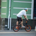 Фотография мужчины на BMX велосипеде с видимыми татуировками на руках и плече, демонстрирующая уличный стиль и современное искусство тела.