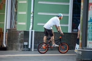 Фотография мужчины на BMX велосипеде с видимыми татуировками на руках и плече, демонстрирующая уличный стиль и современное искусство тела.