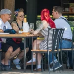 Фотография компании друзей, сидящих за столиком в кафе. У двух женщин видны татуировки на руках.