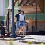 Фотография женщины с татуировкой на плече, стоящей возле кафе. Татуировка выполнена в реалистичном стиле с использованием черных чернил.