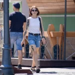 Фотография женщины с татуировкой на плече, идущей рядом с мужчиной по улице. Татуировка выполнена в реалистичном стиле с использованием черных чернил.