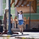 Фото тату зайца на бедре женщины, идущей по улице с черной сумкой. Минималистичный рисунок татуировки, уличная фотография.