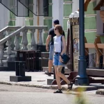 Фото тату зайца на бедре женщины, идущей по улице с черной сумкой. Минималистичный рисунок татуировки, уличная фотография.