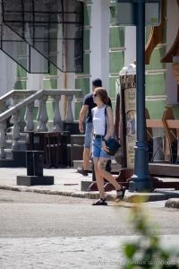Фото тату зайца на бедре женщины, идущей по улице с черной сумкой. Минималистичный рисунок татуировки, уличная фотография.