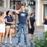 Фото тату: мужчина с татуировкой дракона и другими рисунками на руке, стоящий на улице. Рисунок выполнен в традиционном японском стиле.