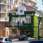 Фото улицы с красивой архитектурой и женщиной с татуировкой на руке. Татуировка выполнена в акварельном стиле.