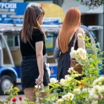 Фото двух женщин на улице, одна из которых демонстрирует татуировку на руке с изображением луны, ветвей и цветов.