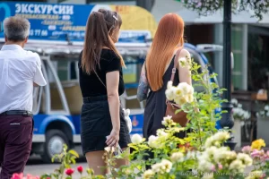 Фото двух женщин на улице, одна из которых демонстрирует татуировку на руке с изображением луны, ветвей и цветов.