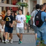 Фотография трех человек на улице, один из которых демонстрирует татуировку на руке. Современный уличный стиль, татуировки, повседневная одежда.