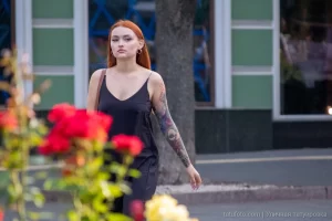 Фото тату на руке девушки: детализированный рисунок с изображением лица, цветов и узоров, выполненный в ярких цветах, на фоне цветущих роз.