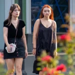 Фотография двух девушек, идущих по улице, одна из которых имеет татуировку на плече. Тату выполнено в темных тонах и частично скрыто одеждой.