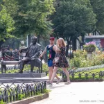 Фото тату на руке и ноге мужчины, идущего с девушкой в парке. Видны небольшие, но детализированные рисунки, выполненные в черном цвете.
