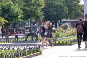 Фото тату на руке и ноге мужчины, идущего с девушкой в парке. Видны небольшие, но детализированные рисунки, выполненные в черном цвете.