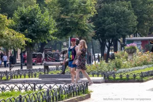 Фото тату на руке и ноге мужчины, идущего с девушкой в парке. Видны небольшие, но детализированные рисунки, выполненные в черном цвете.