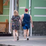 Фото тату на руке и ноге мужчины, идущего с девушкой. Видны небольшие, но детализированные рисунки, выполненные в черном цвете.