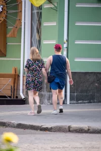 Фото тату на руке и ноге мужчины, идущего с девушкой. Видны небольшие, но детализированные рисунки, выполненные в черном цвете.