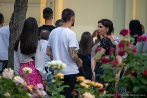 Фотография уличной татуировки на руке и ноге мужчины. Видны детализированные рисунки в стиле графика, выполненные черными чернилами. На заднем плане люди и цветы.