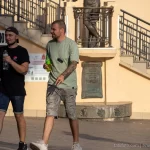 Фотография мужчины с рукавом татуировок, идущего по улице в солнечный день. Татуировки выполнены в стиле блэкворк и покрывают всю руку.
