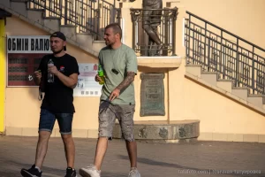 Фотография мужчины с рукавом татуировок, идущего по улице в солнечный день. Татуировки выполнены в стиле блэкворк и покрывают всю руку.