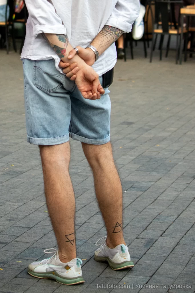 Парная татуировка с перечеркнутыми треугольниками внизу ног парня 2