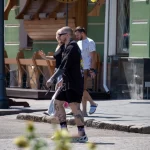 Фото тату на ногах и рукаве мужчины, идущего по улице. Видны детализированные рисунки, выполненные в реалистичном стиле.