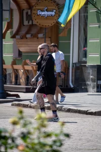 Фото тату на ногах и рукаве мужчины, идущего по улице. Видны детализированные рисунки, выполненные в реалистичном стиле.