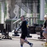 Фото тату на руках и ногах мужчины, идущего по улице. Видны детализированные рисунки на предплечьях и голенях, выполненные в реалистичном стиле.