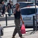 Фотография мужчины с татуировками на руке, идущего по улице и разговаривающего по телефону. Вид сбоку, солнечный день, городской пейзаж.
