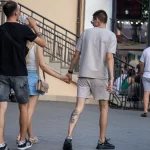 Фото пары с татуировками: у мужчины тату на ноге, у женщины - на руке. Они держатся за руки на улице.