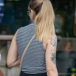 Фотография крупным планом татуировки на плече девушки, изображающей цветы и бабочек в черно-серых тонах.