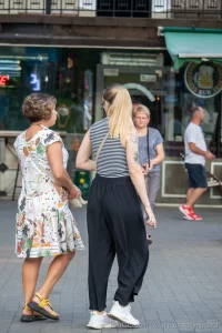 Фотография девушки с татуировкой на плече, изображающей цветы и бабочек в черно-серых тонах. Девушка идет по улице.
