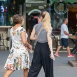 Фотография девушки с татуировкой на плече, идущей по улице. Татуировка выполнена в черно-серых тонах и изображает цветочный узор.