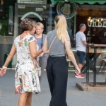 Фотография девушки с татуировкой на плече, идущей по улице. Татуировка выполнена в черно-серых тонах и изображает цветочный узор.