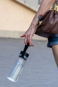 Крупный план руки женщины с акварельной татуировкой в виде спирали. Видна сумка и часть одежды. Уличная фотография.