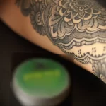 Фото татуировки на руке женщины: мандала в стиле dotwork, зеленый крем для татуировки. Детализированный рисунок татуировки, выполненный точками.