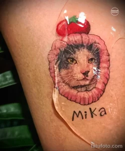 Фотография татуировки кота в клубничке на руке. Акцент на ярких цветах, милом дизайне и детализации.