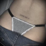 Фото тату: простая надпись "Love Me" с сердечком, выполненная тонкой линией на коже, минималистичный стиль.