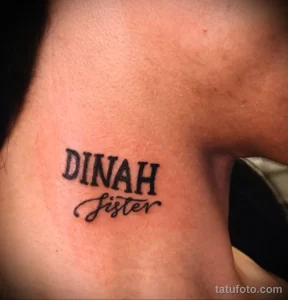 Фото тату на женской шее: надпись "DINAH Sister", выполненная черными чернилами в каллиграфическом стиле. Персонализированная и эмоциональная татуировка.